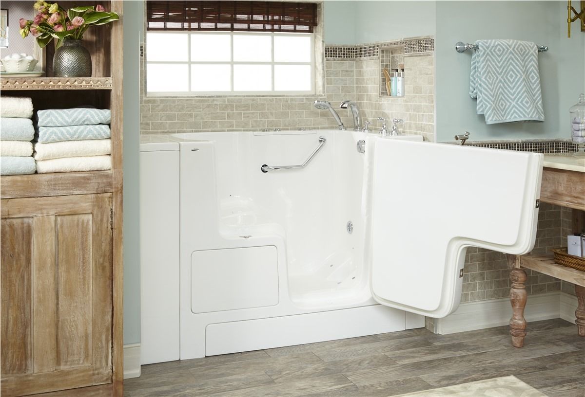 Accessible bathroom with walk-in tub, white fixtures, and wooden storage cabinet