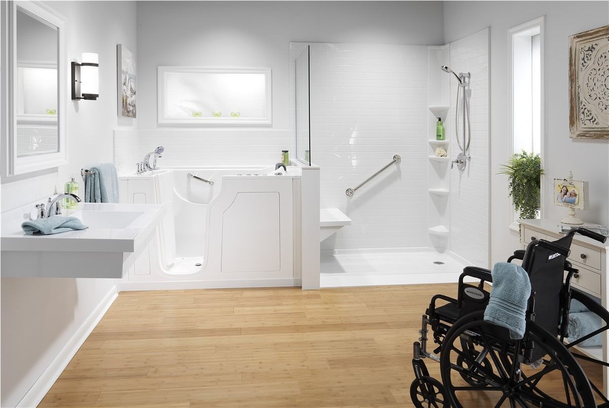 Bright accessible bathroom with white fixtures, wood floor, and a wheelchair in the foreground.
