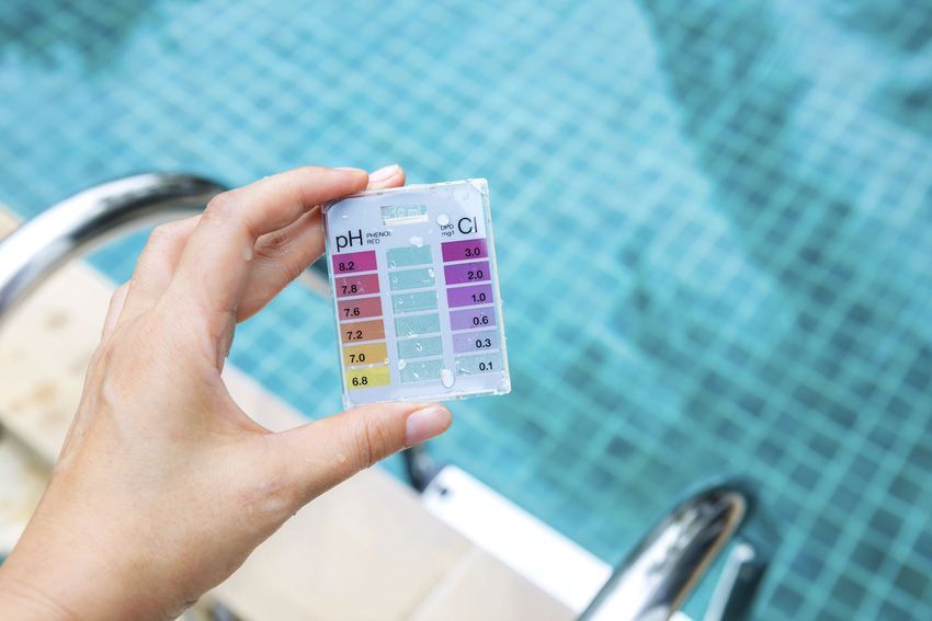 A person is holding a test strip in front of a swimming pool.