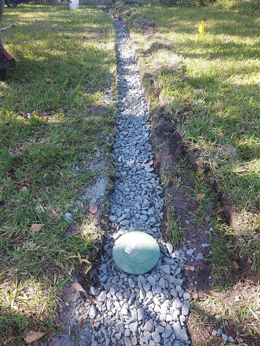 A rock is sitting in the middle of a gravel path in the grass.