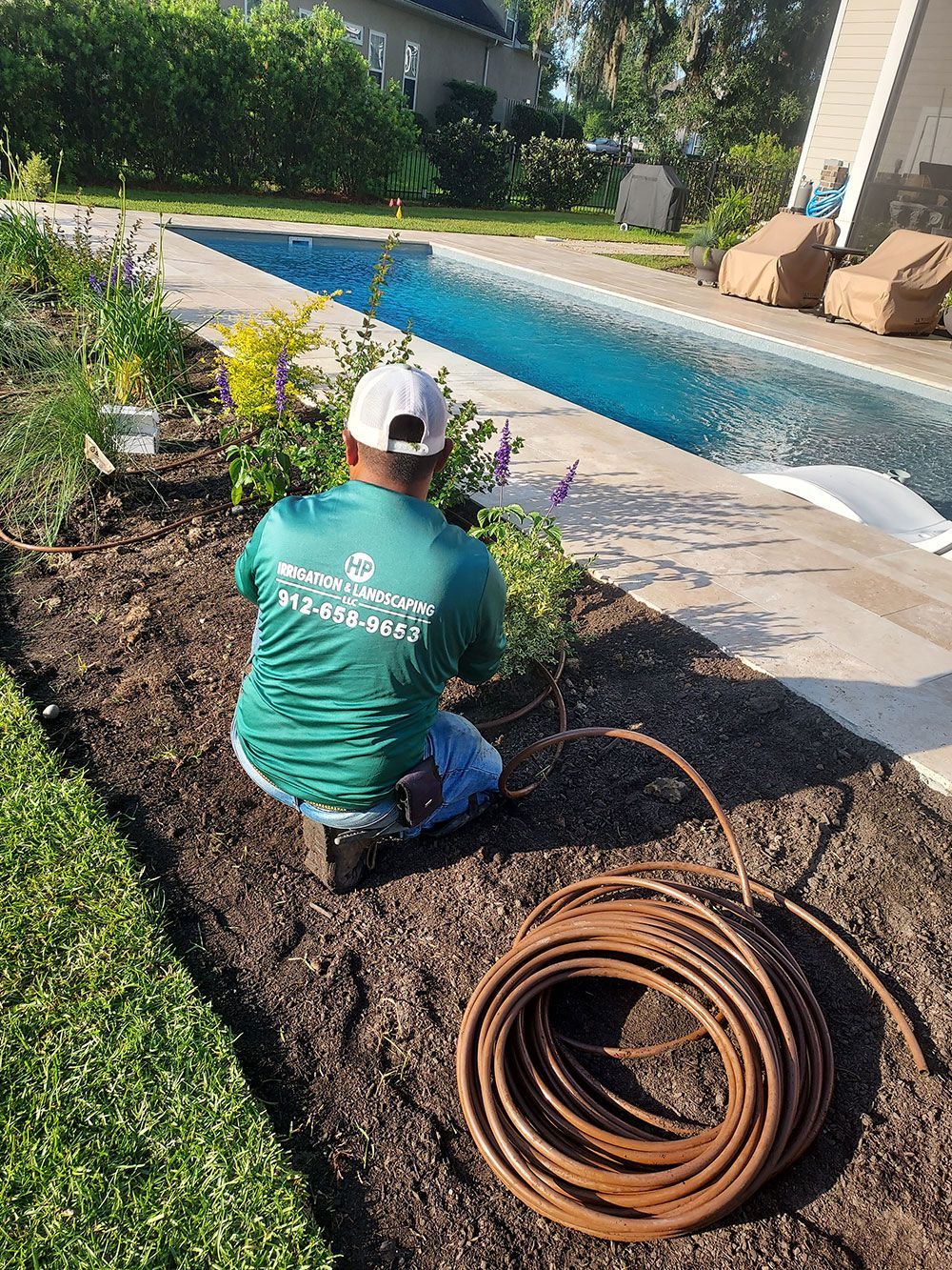 A man is kneeling down in a garden next to a pool.