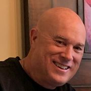 A bald man is smiling in front of a picture on a wall.