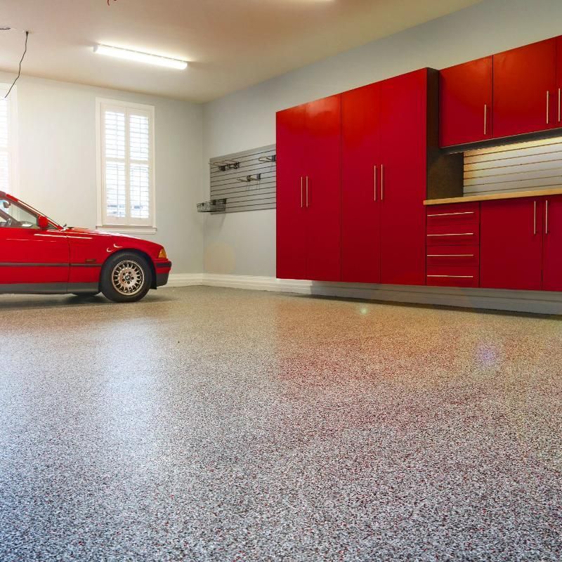 A red car is parked in a garage with red cabinets