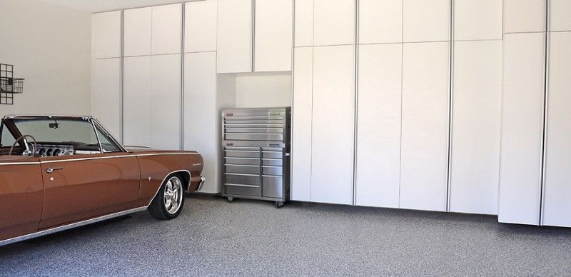 A brown car is parked in a garage with white cabinets.