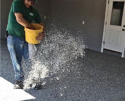 A man in a green shirt is pouring a yellow bucket of water on a carpeted floor.