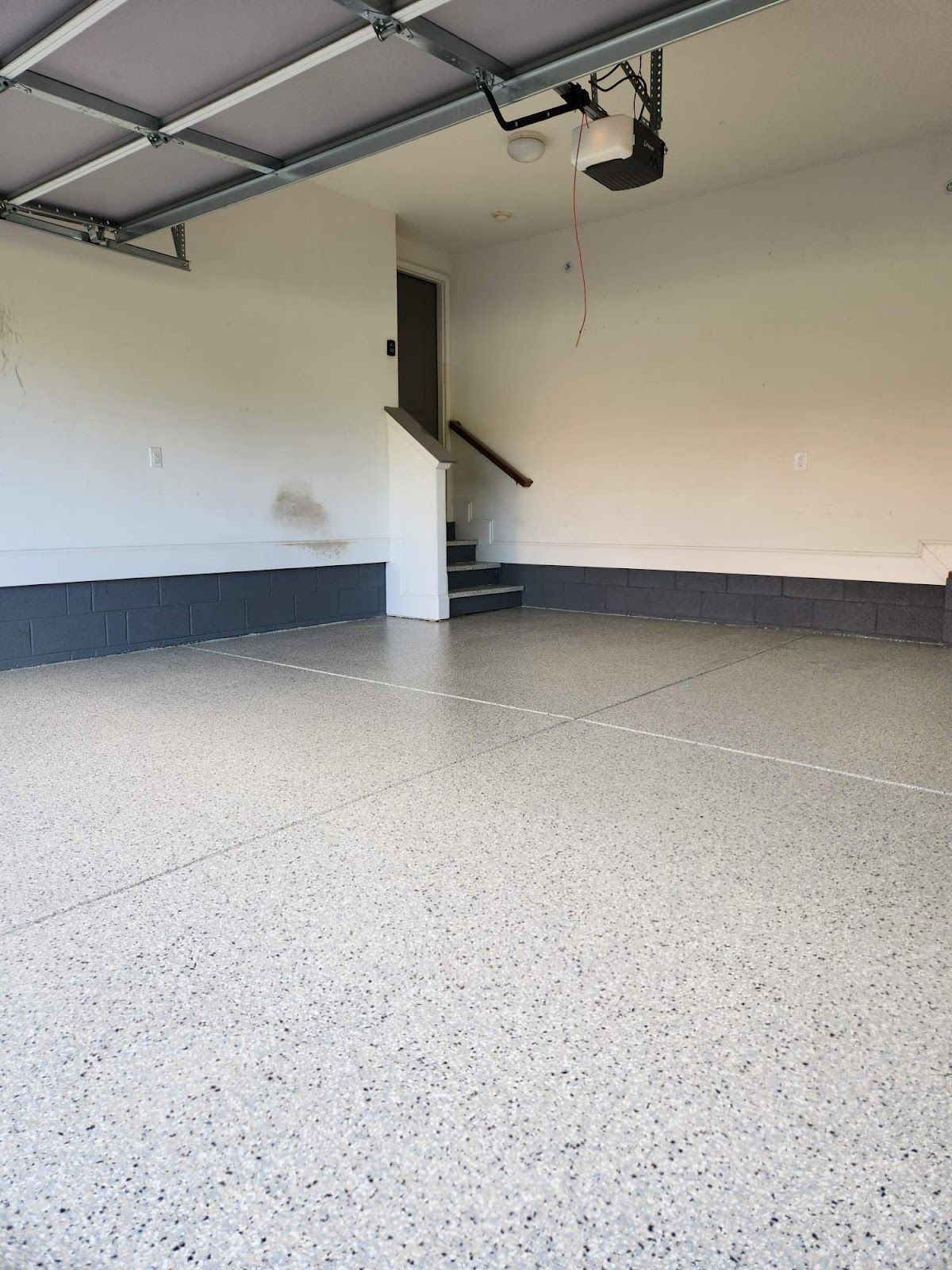 An empty garage with a staircase and a garage door opener.