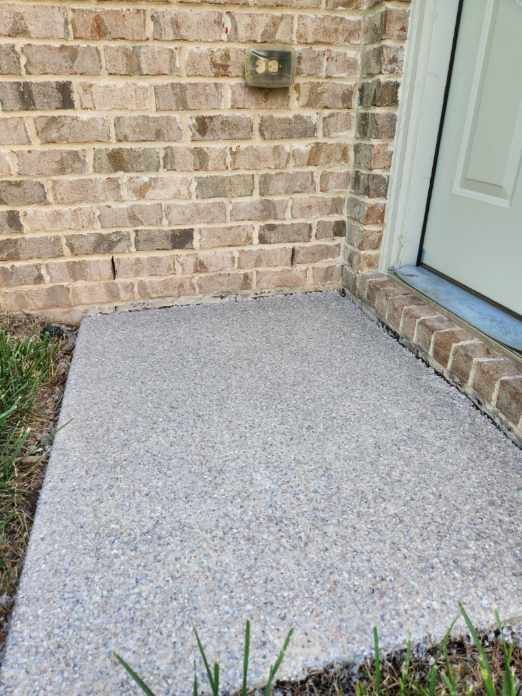 A brick wall with a concrete walkway in front of it.