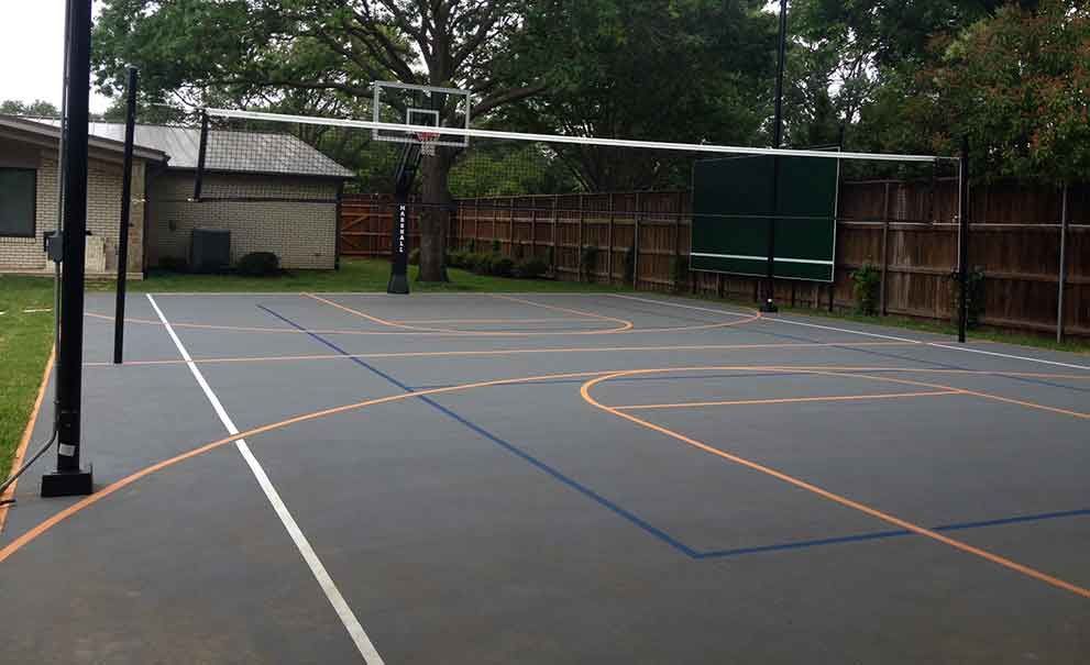 A basketball court with a volleyball net in the backyard of a house.