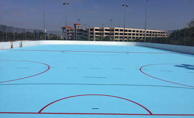 A blue ice rink with red lines and a building in the background