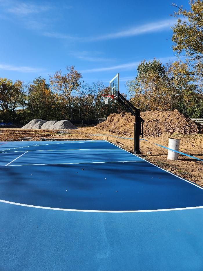 A blue basketball court with a basketball hoop in the middle of a dirt field.
