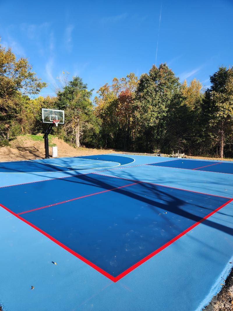 A blue and red basketball court with trees in the background.