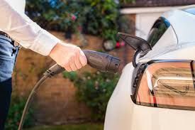 Person charging a white electric car with a plug at an outdoor station