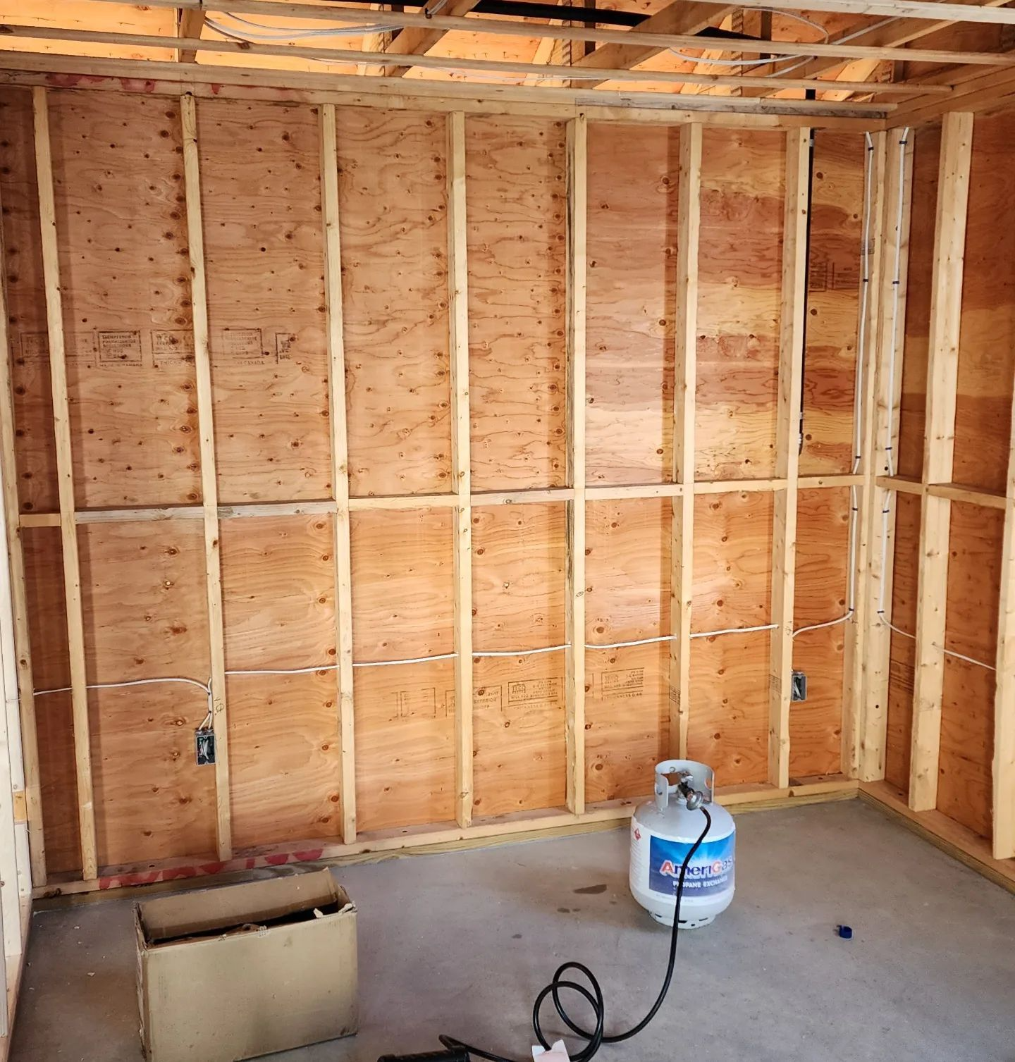 Unfinished room with exposed wooden framing, plywood walls, a concrete floor, and a propane tank on the floor.