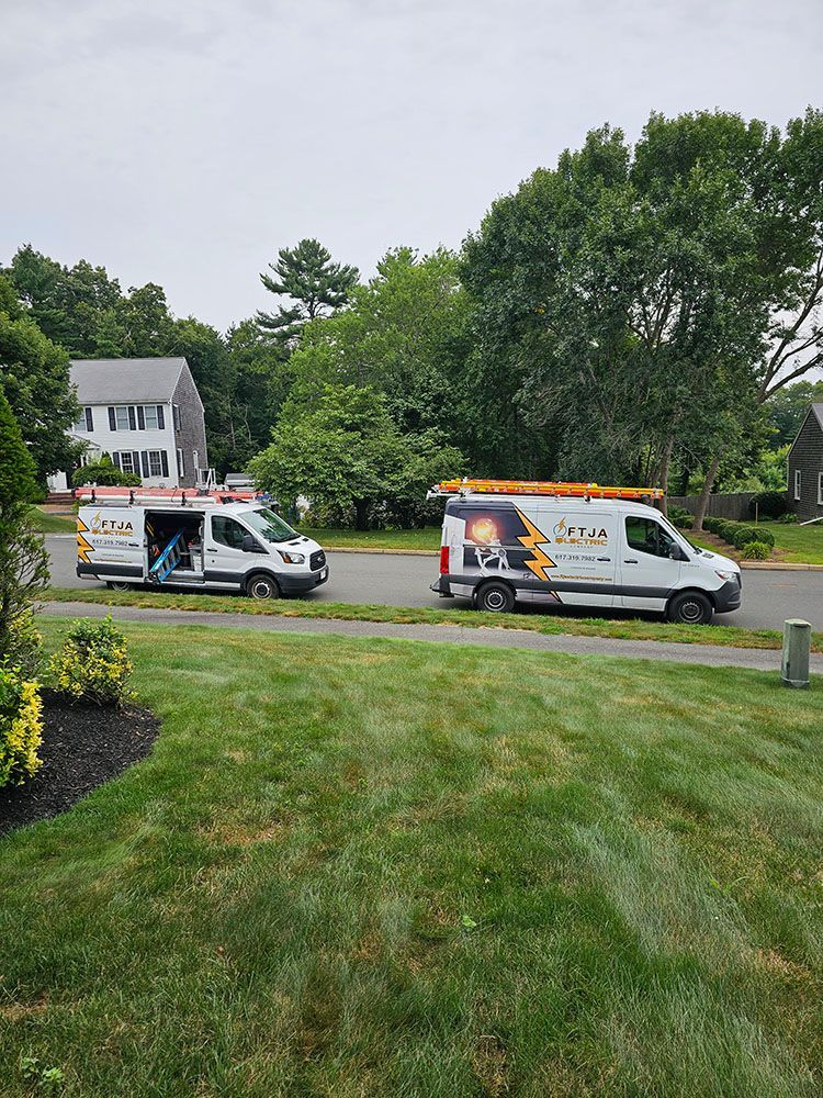Two white service vans parked by a grassy lawn and trees on a cloudy day