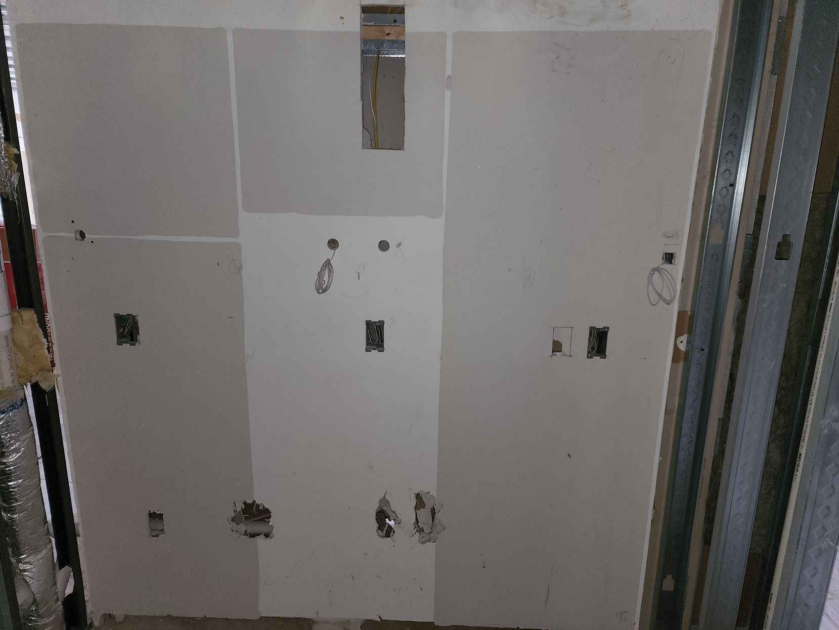 Partially tiled bathroom wall with plumbing outlets and electrical boxes during renovation
