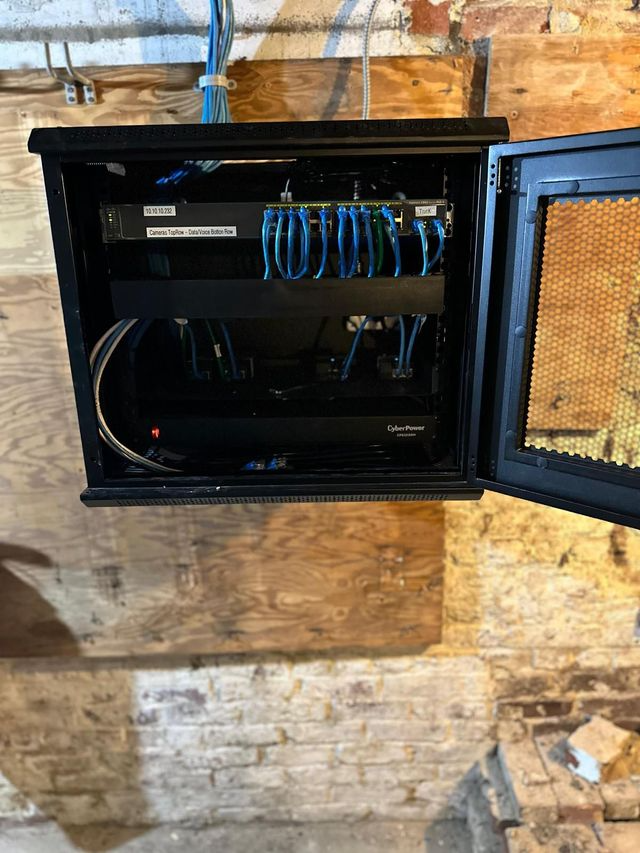 Open wall-mounted network cabinet with blue Ethernet cables and equipment inside, mounted on a rough brick wall