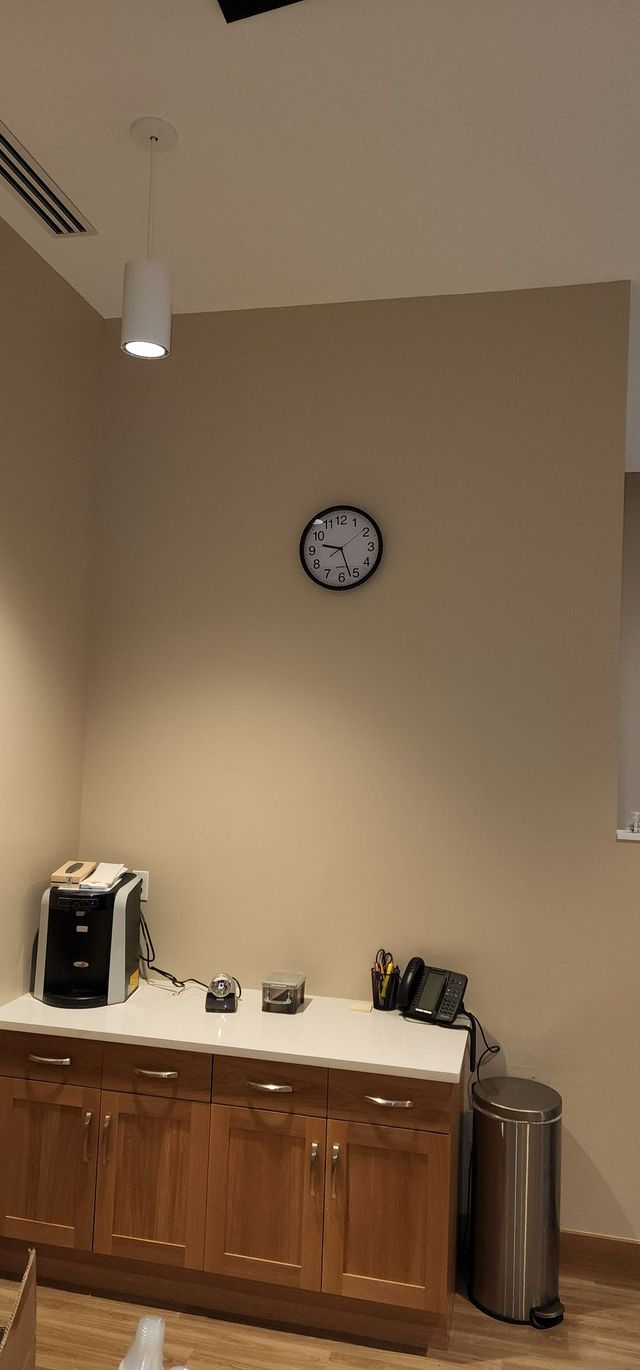 Quiet office corner with wall clock, coffee station, wooden cabinet, and a trash can