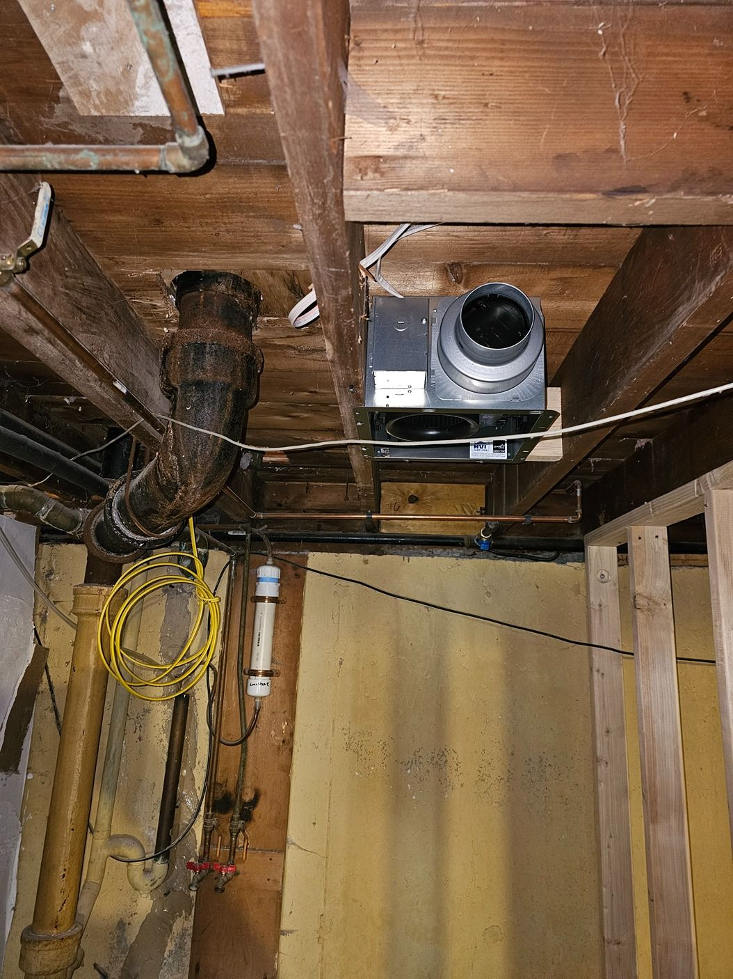 Exposed ceiling crawlspace with ductwork, pipes, and a mounted ventilation fan.