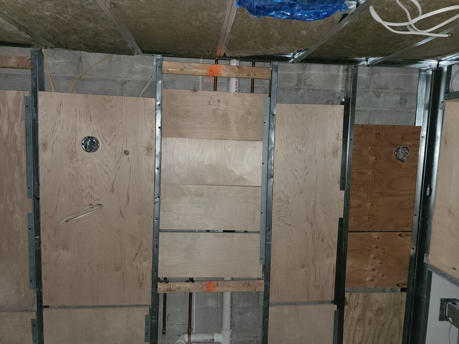 Plywood and drywall access panels in a wall cavity with exposed framing and insulation.