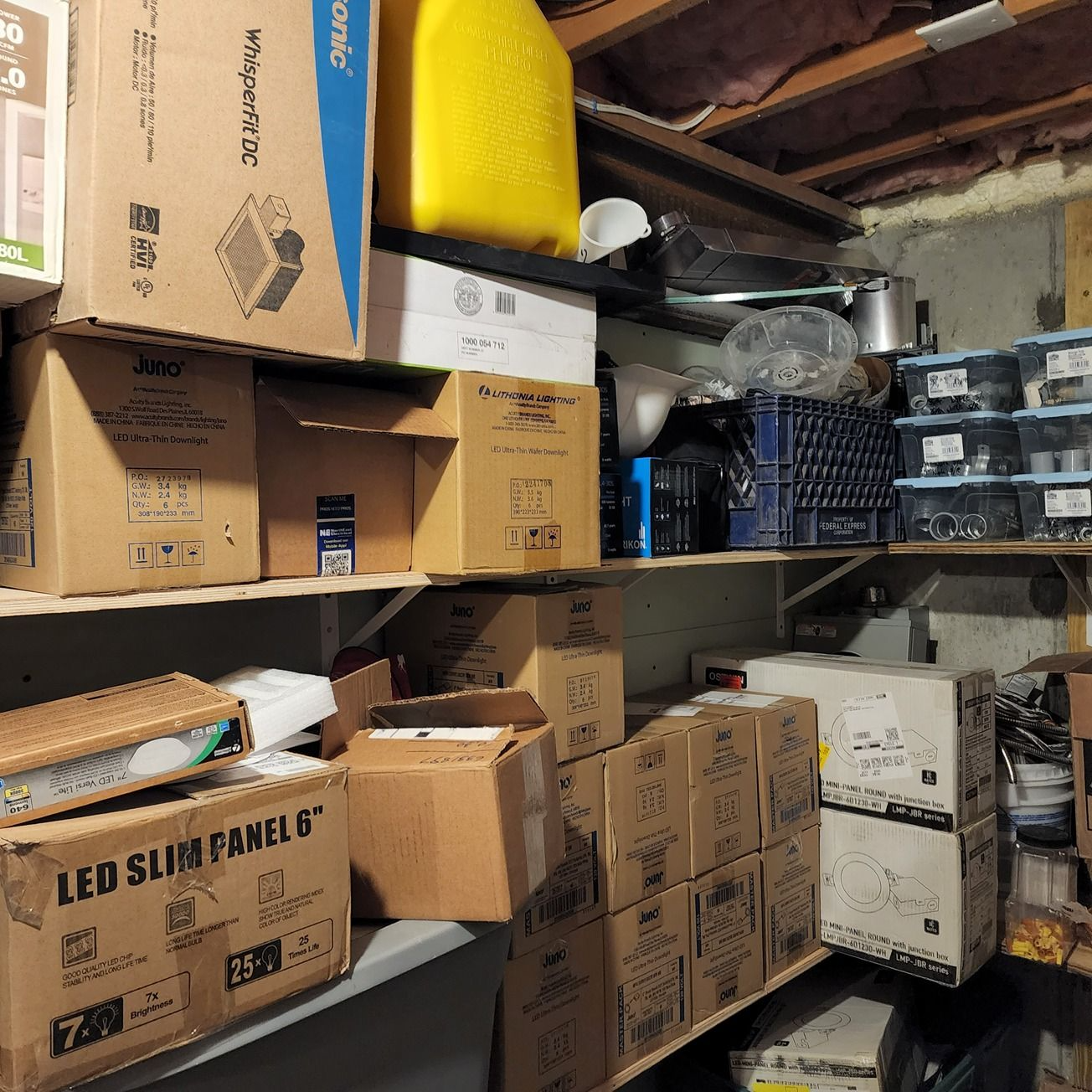 Cluttered storage room with stacked cardboard boxes, plastic bins, and shelves filled with packed household items.