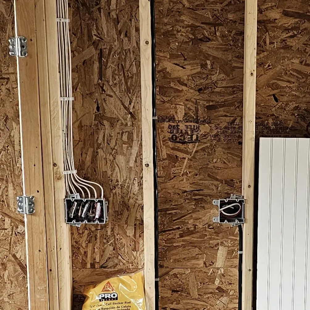Partially finished wall framing with exposed wiring, electrical boxes, and a white panel on the right