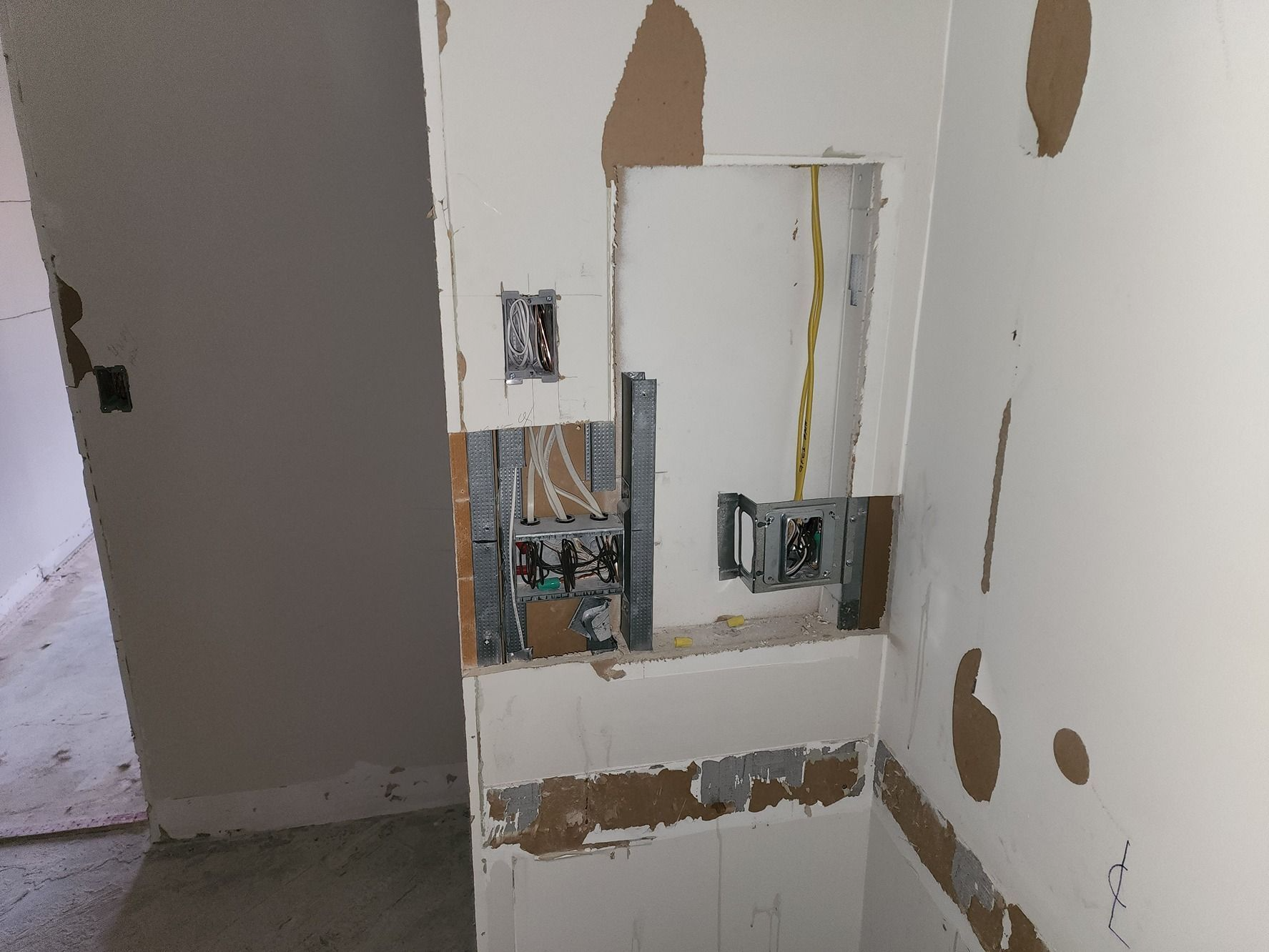 Exposed electrical boxes and wiring in a damaged wall with peeled paint and drywall patches