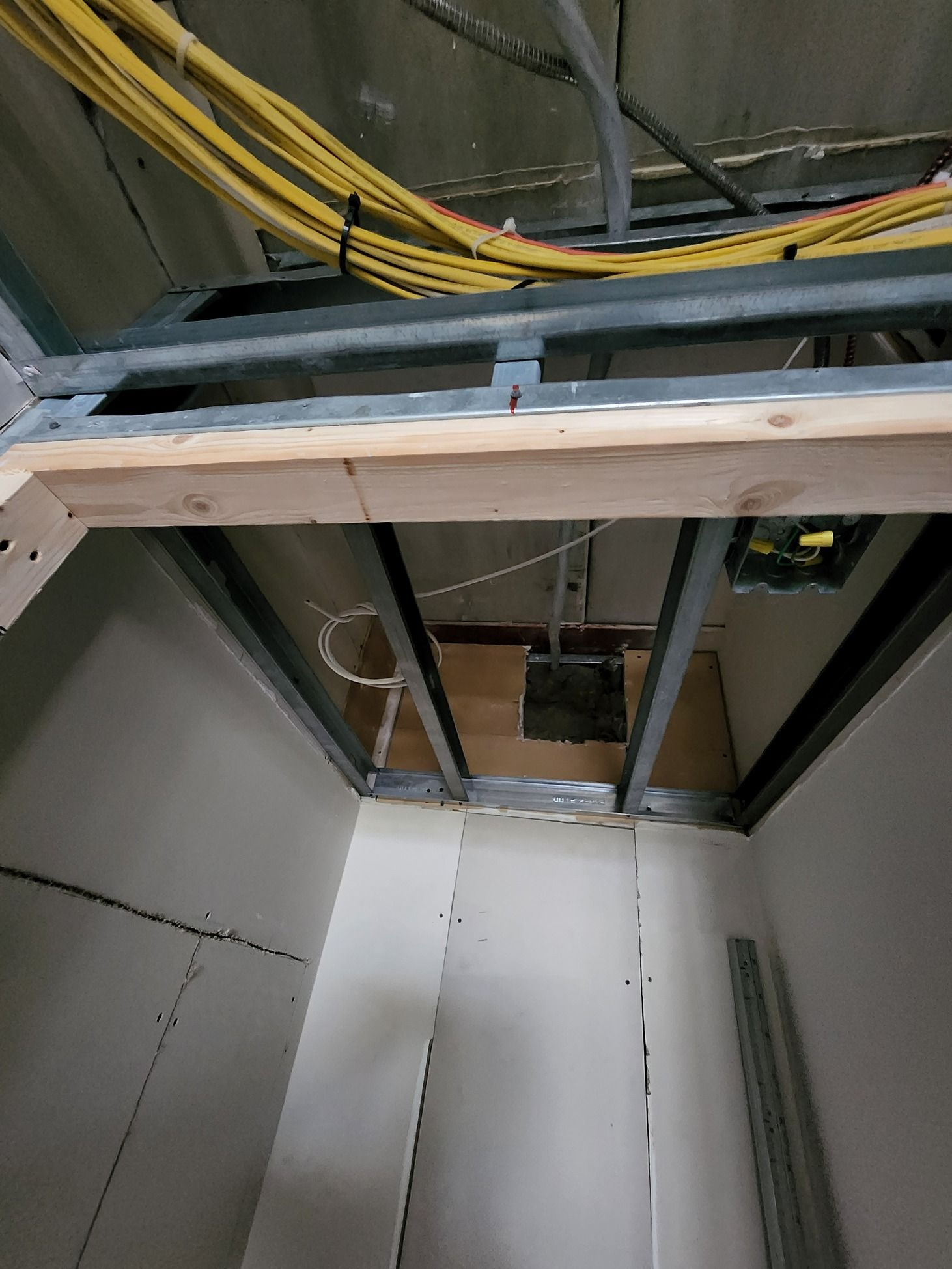 Interior construction site with exposed ceiling beams, yellow cables, and unfinished wall panels.