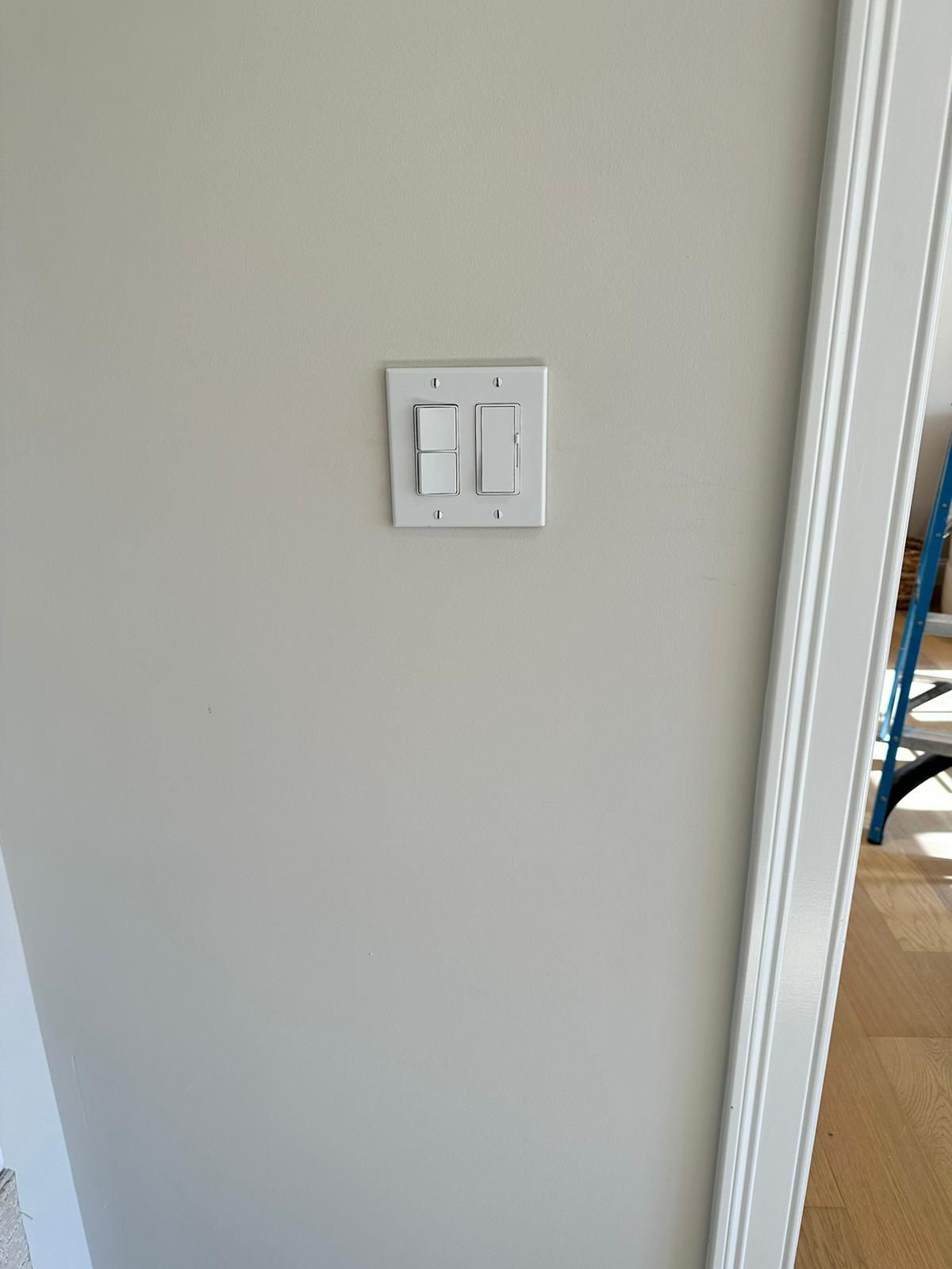 White double light switch on a beige wall beside a doorway.