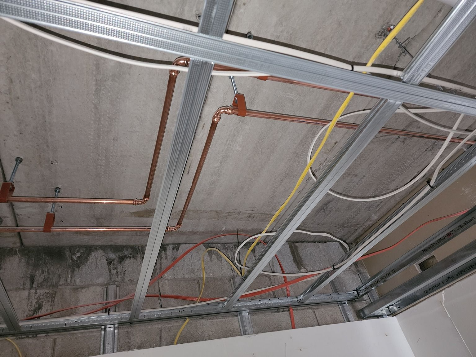 Ceiling with exposed metal framing, electrical conduit, and hanging cables in a construction area