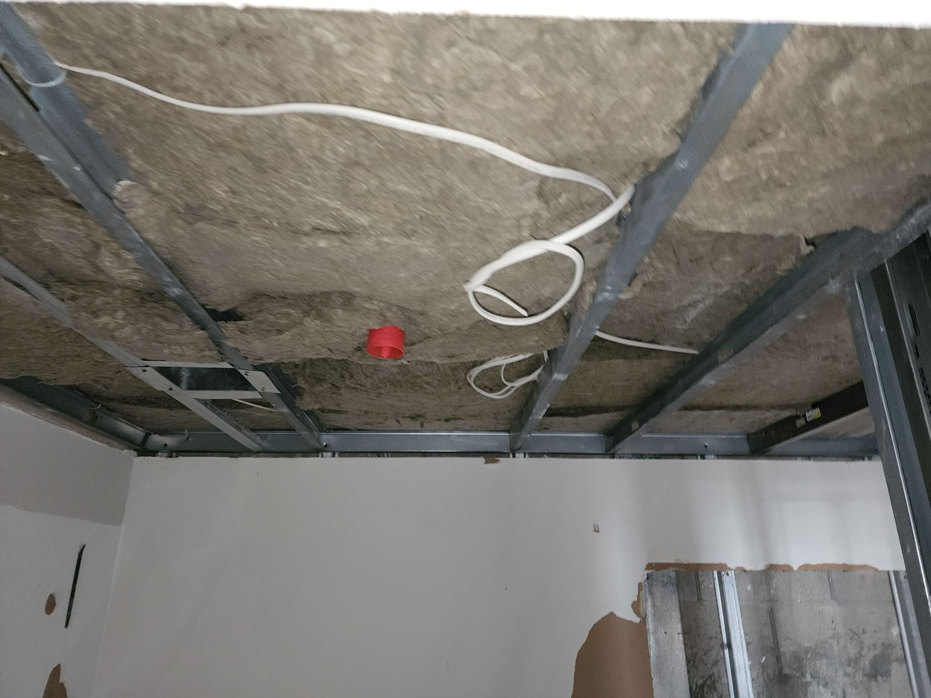 Ceiling under construction with exposed insulation, wires, and metal framing above unfinished walls.