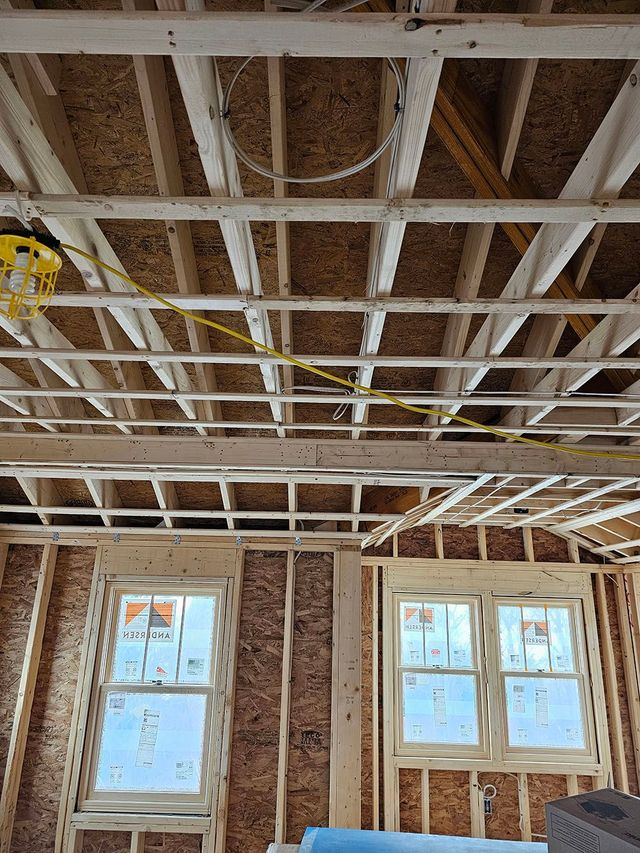 Interior of a room under renovation with exposed ceiling joists, wiring, and two windows.