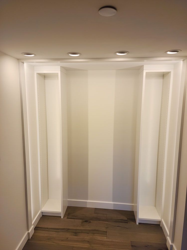 Empty white closet with built-in shelves, recessed ceiling lights, and wood flooring