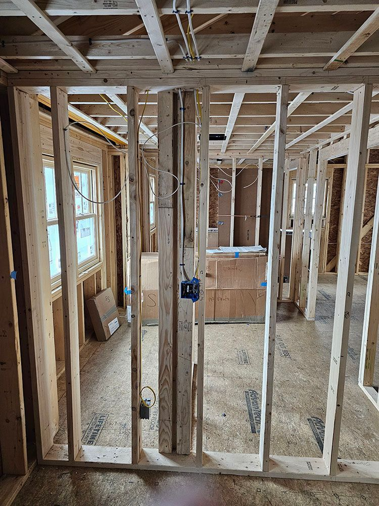 Framed house interior under construction with exposed studs, ceiling joists, windows, and rough wiring.