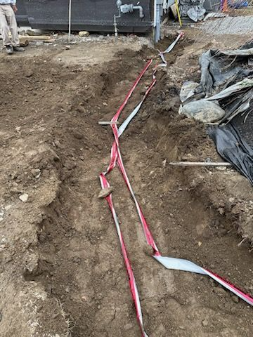 Dug trench at a construction site with red ribbon tape running along the dirt floor and sides.
