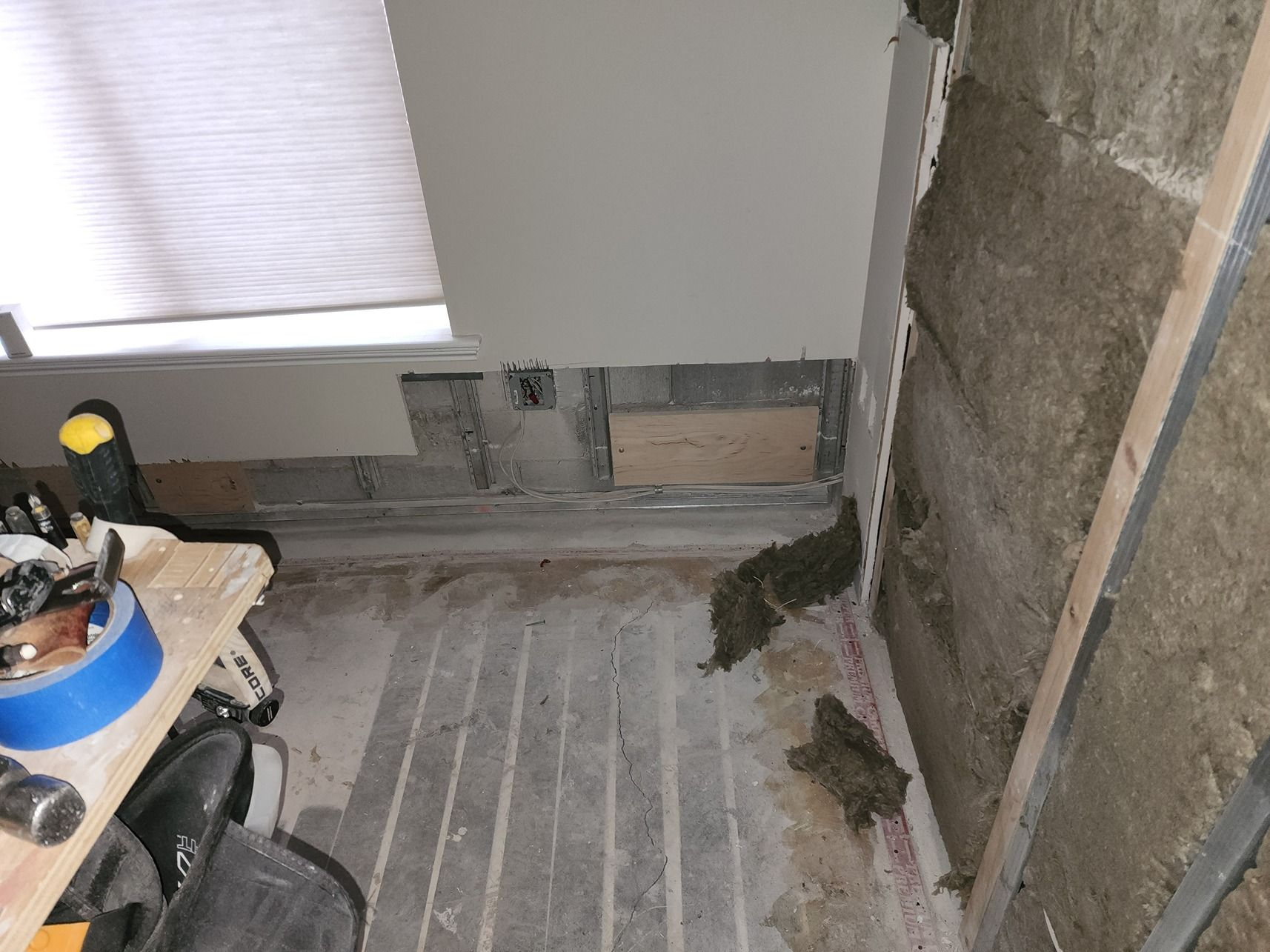Partially renovated room with exposed wall studs, insulation, and unfinished flooring near a window