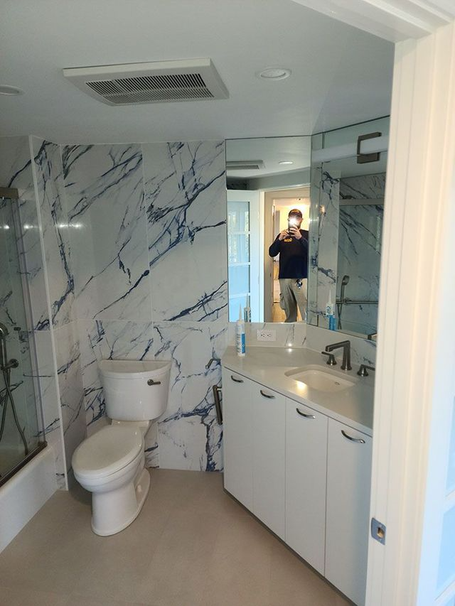 Modern bathroom with marble-pattern walls, toilet, vanity sink, mirror, and shower.