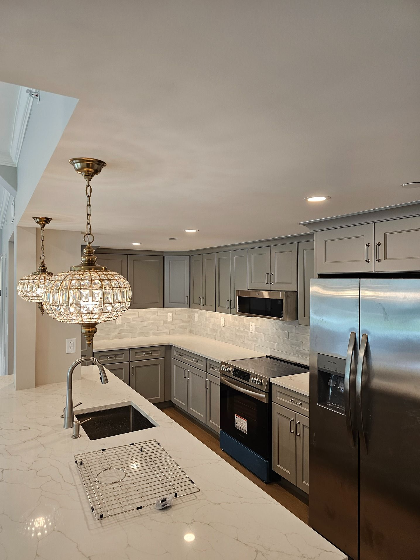 Modern kitchen with white cabinets, stainless steel appliances, marble island, and hanging crystal chandelier