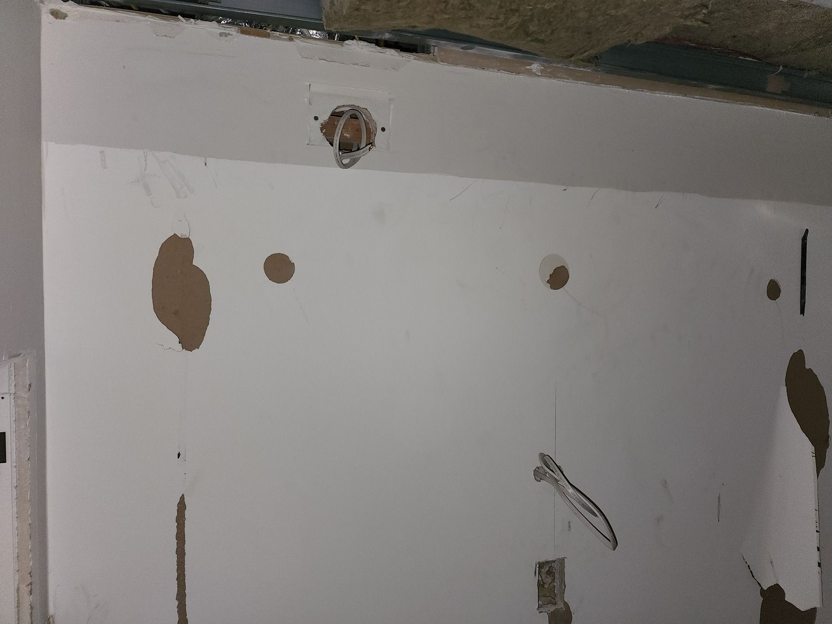 Partially painted white wall with several holes and peeling areas near the ceiling
