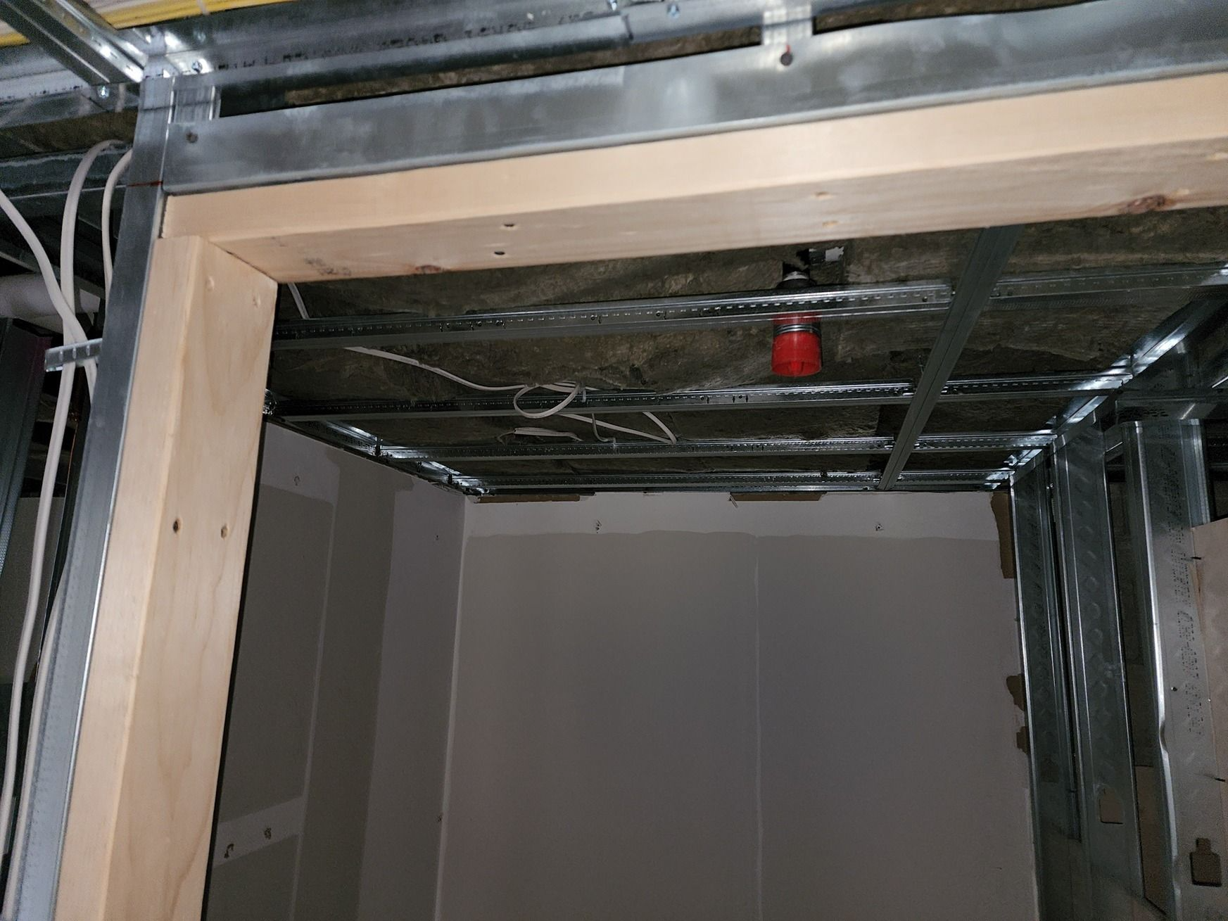 Wood-framed opening in unfinished building interior with exposed metal ceiling and red sprinkler valve