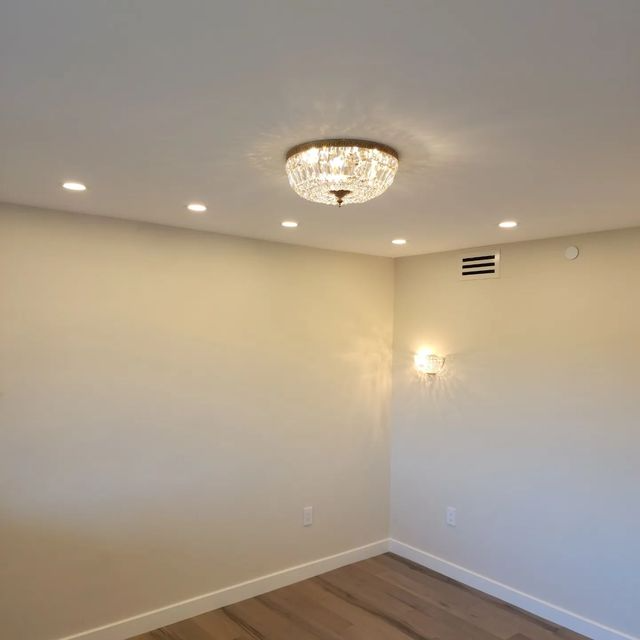 Empty cream-colored room with hardwood floor, recessed lights, and a chandelier ceiling fixture