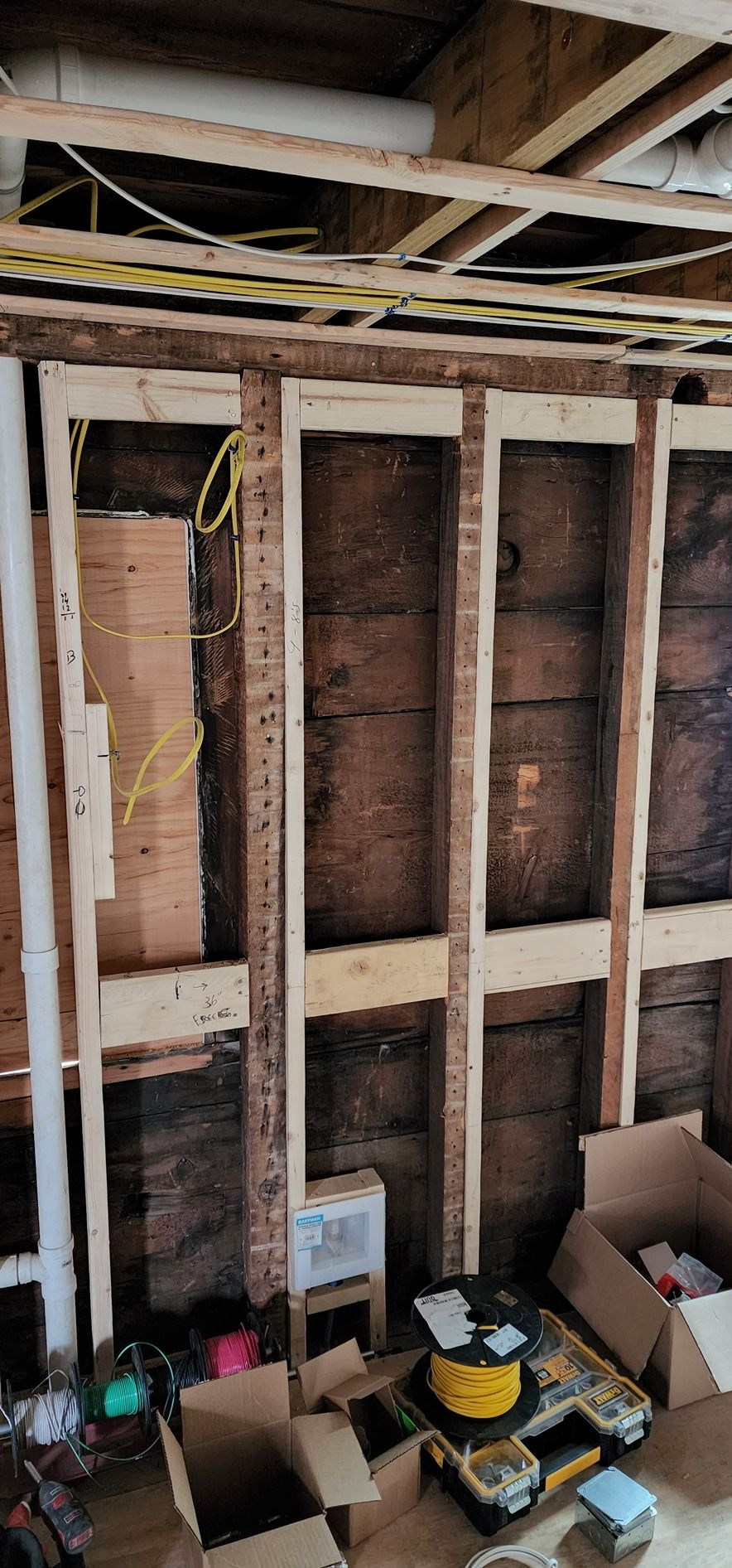 Exposed wall studs and unfinished drywall in a renovation area, with tools and boxes on the floor.
