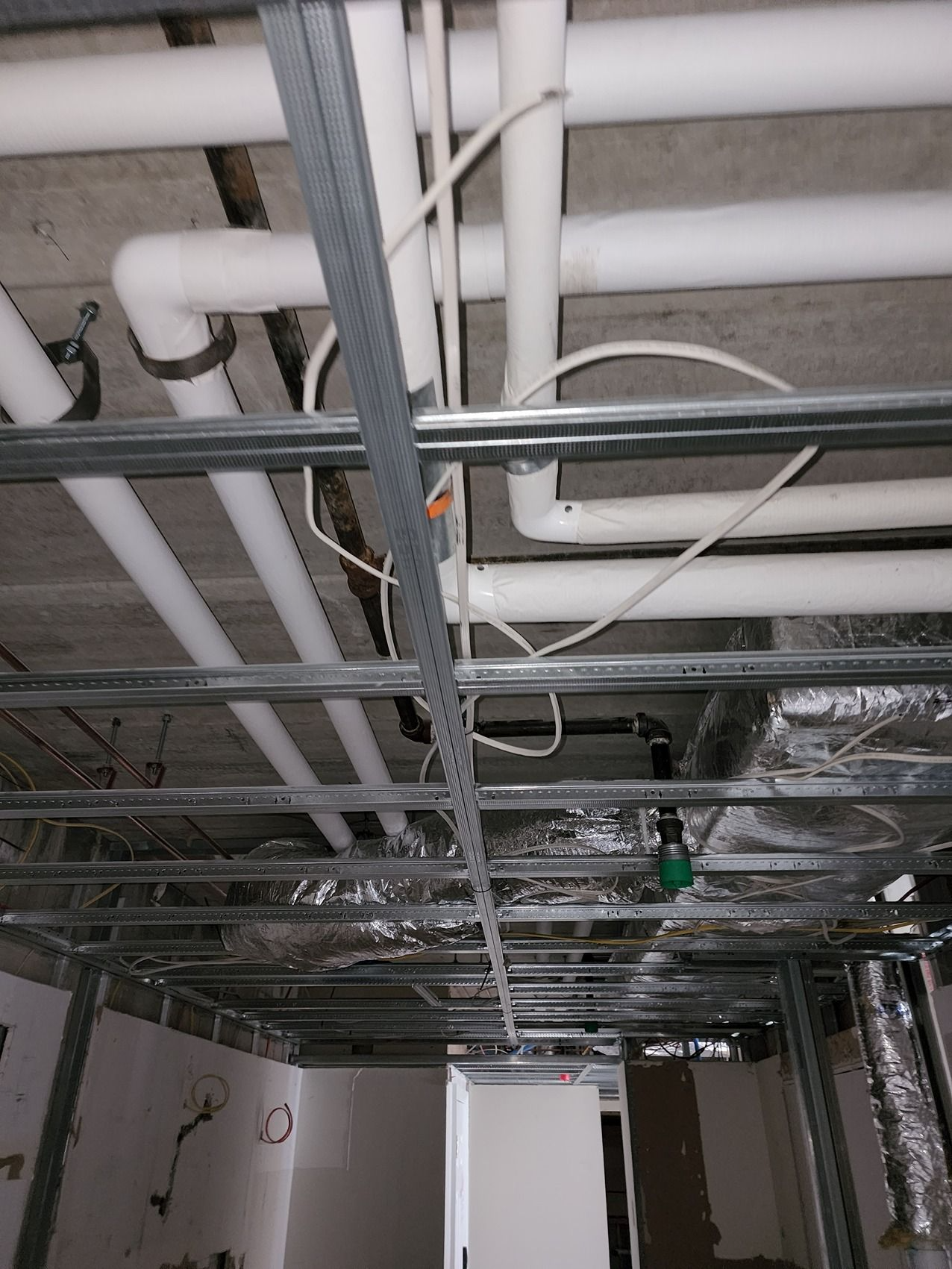 Ceiling utility space with exposed pipes, ducts, conduit, and hanging lights under construction