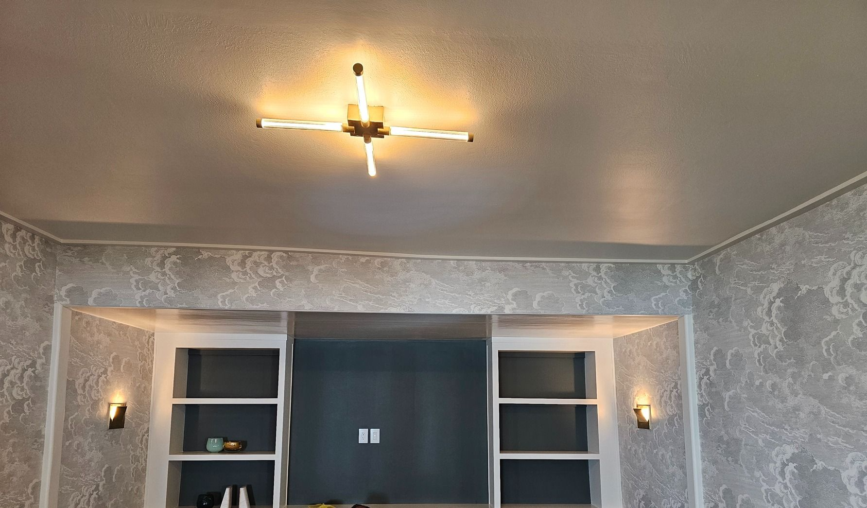 Modern room with patterned gray wallpaper, built-in shelves, wall sconces, and a lit ceiling fan.