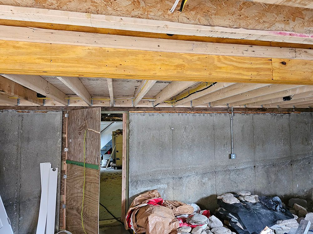 Basement under construction with exposed wooden beams, concrete walls, and piles of debris on the floor
