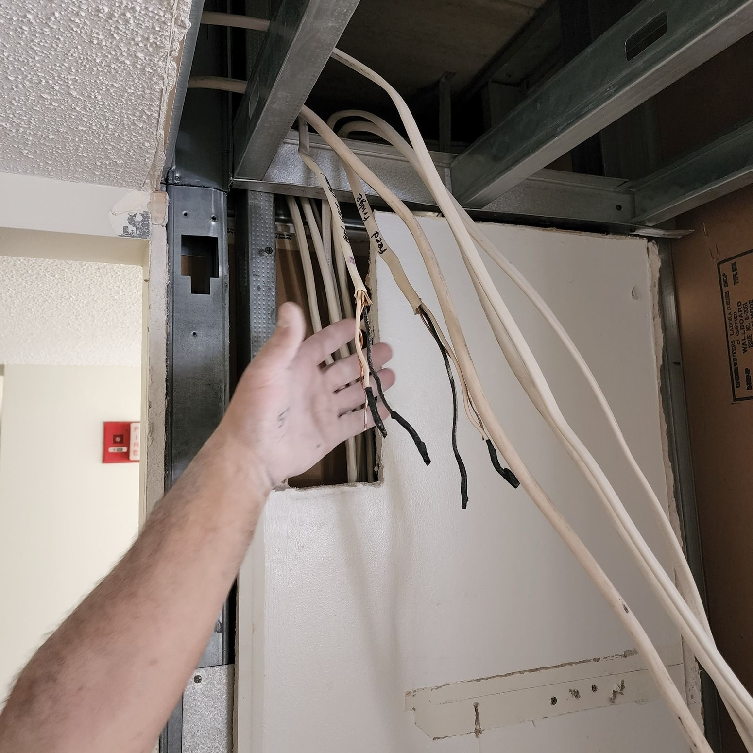 Hand reaching toward exposed electrical cables in an unfinished wall cavity