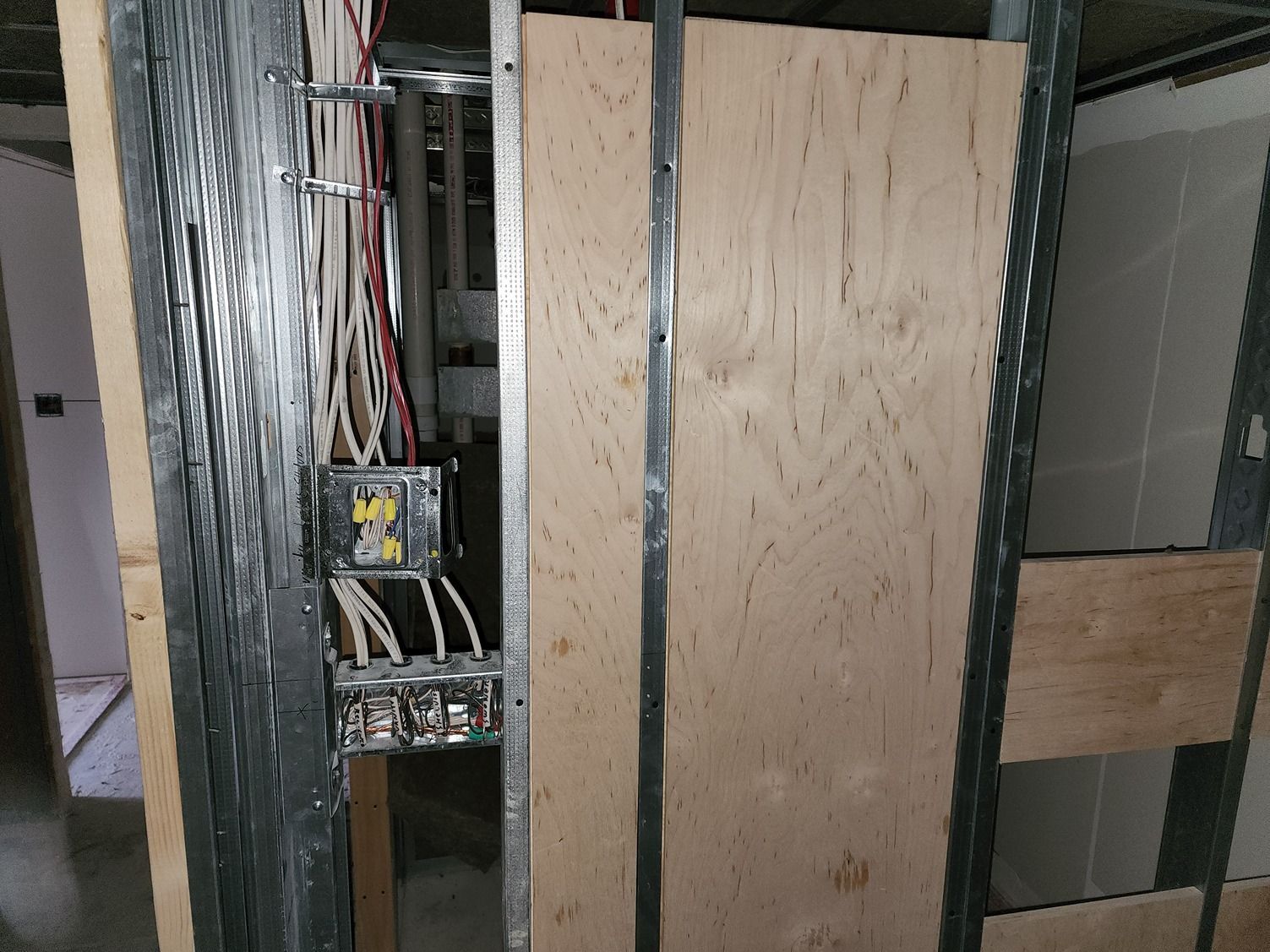 Construction wall with exposed wiring, electrical panel, and plywood-covered openings in a building frame