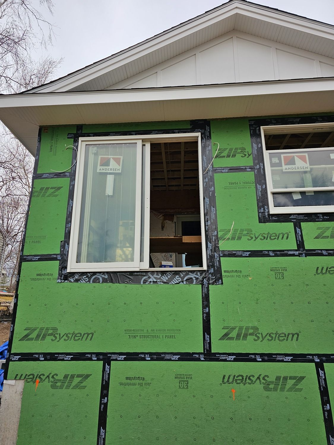 Partially finished house exterior with green sheathing and open windows under a white gable roof