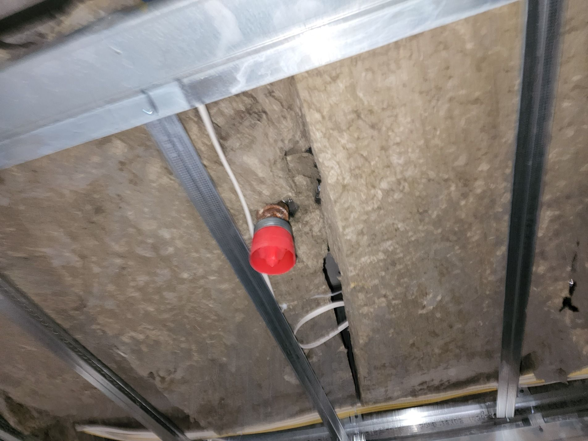 Ceiling with exposed insulation, metal framing, and a red-capped pipe or fitting through a damaged section