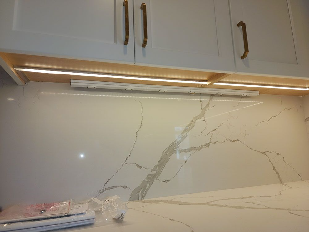 Kitchen counter with cracked marble backsplash and under-cabinet lighting beneath white cabinets.