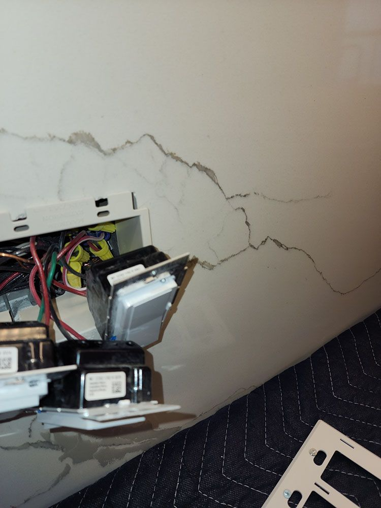 Exposed electrical box in a cracked wall with wires and devices hanging out